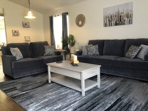 Un salon moderne avec deux canapés gris foncé, une table basse blanche et un tapis à motifs.
