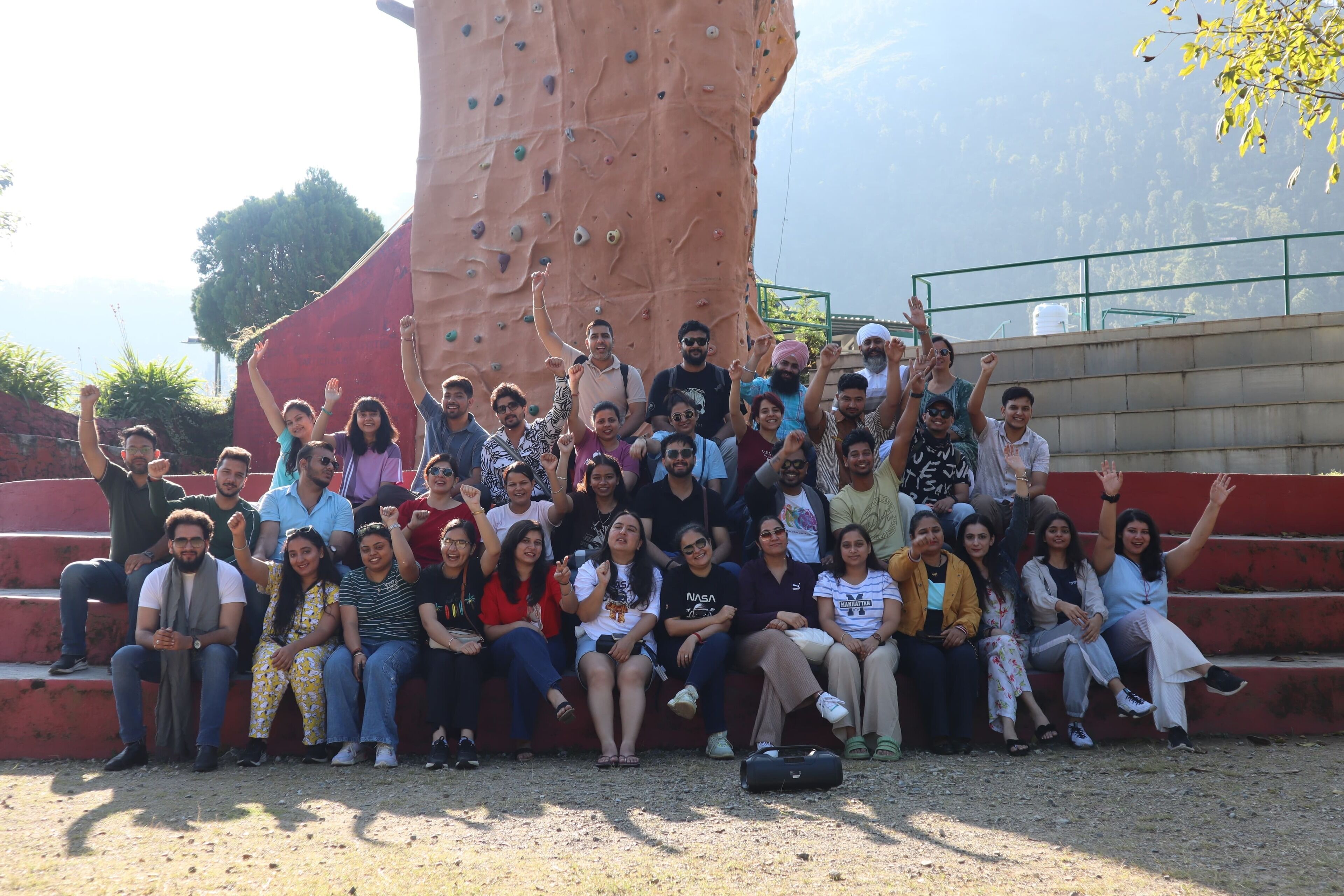 A group of people sitting on outdoor steps with a large rock climbing wall in the background.