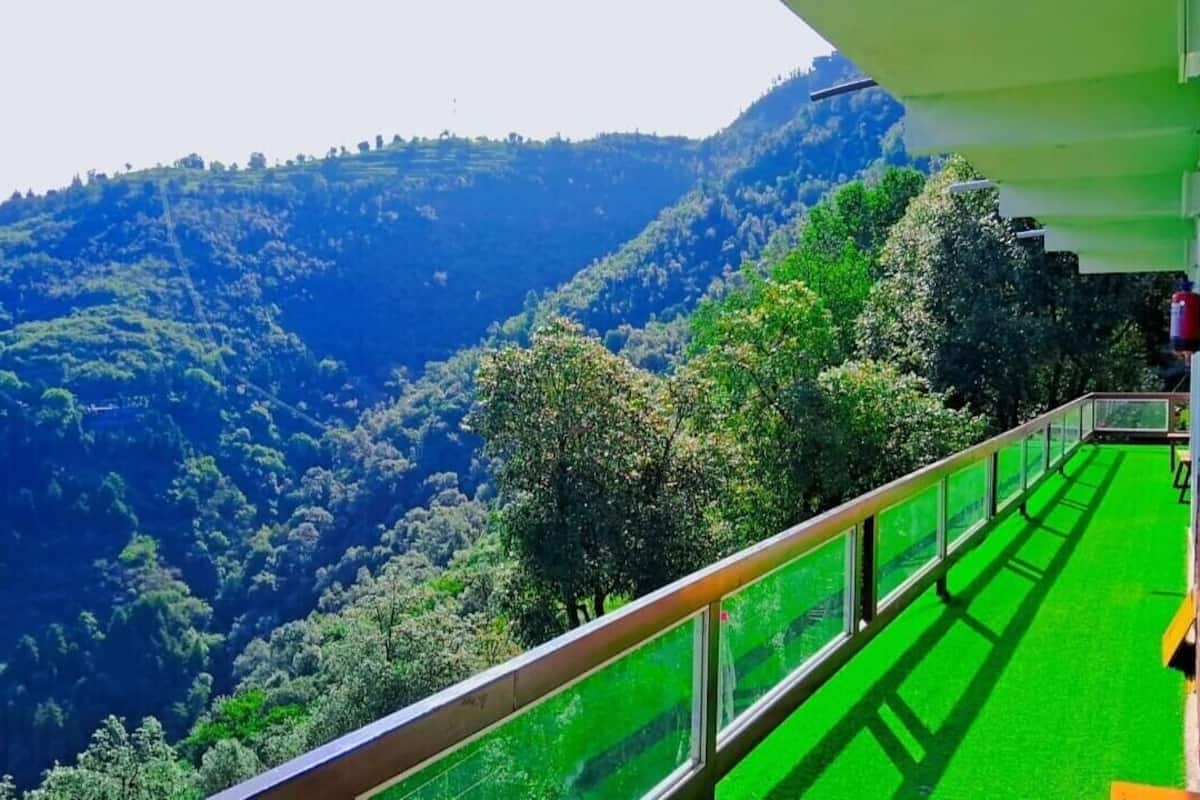 A balcony with a green floor, overlooking a lush valley with dense trees and hills.
