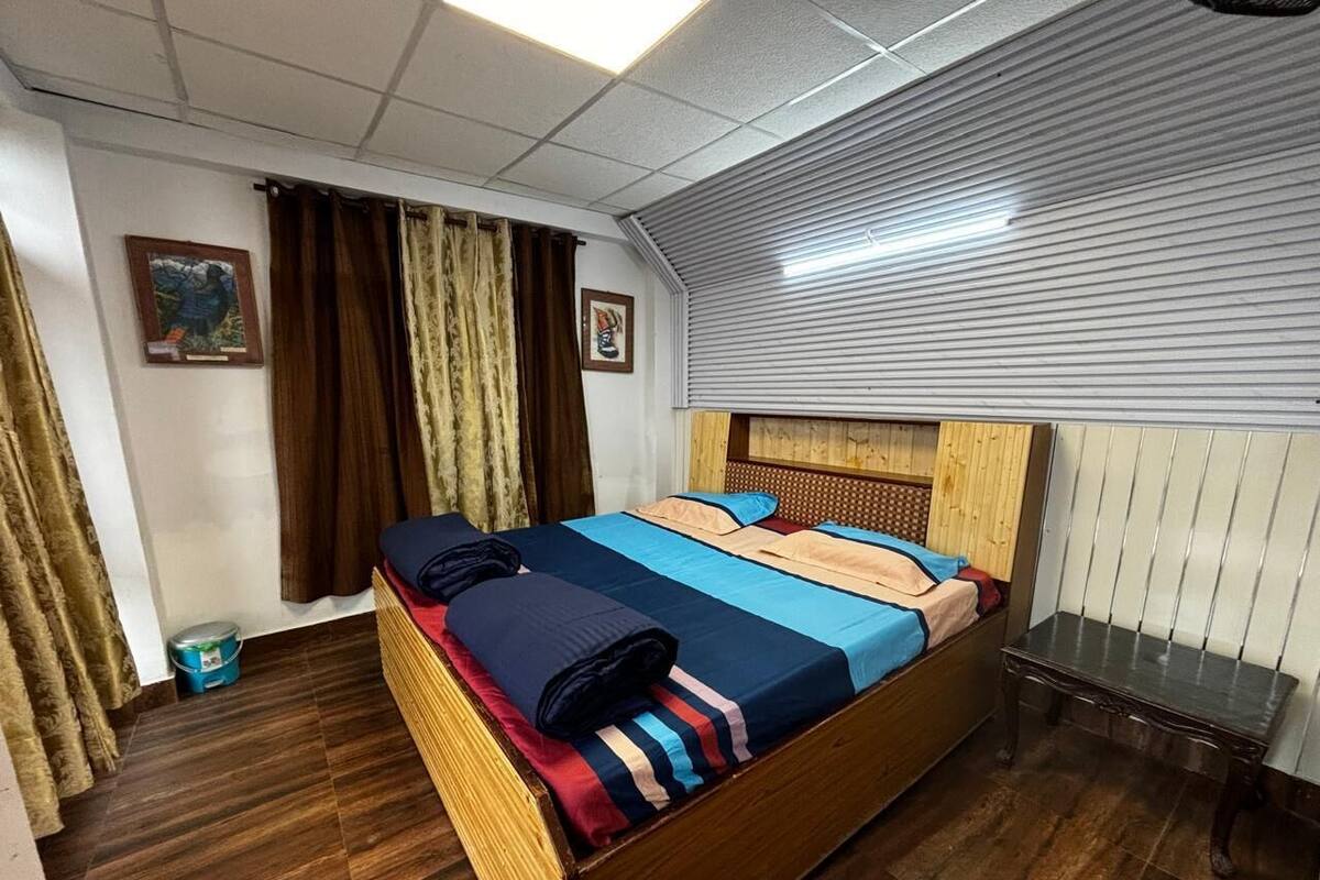 A hotel room with a wooden bed, a small table, and a window with blinds.