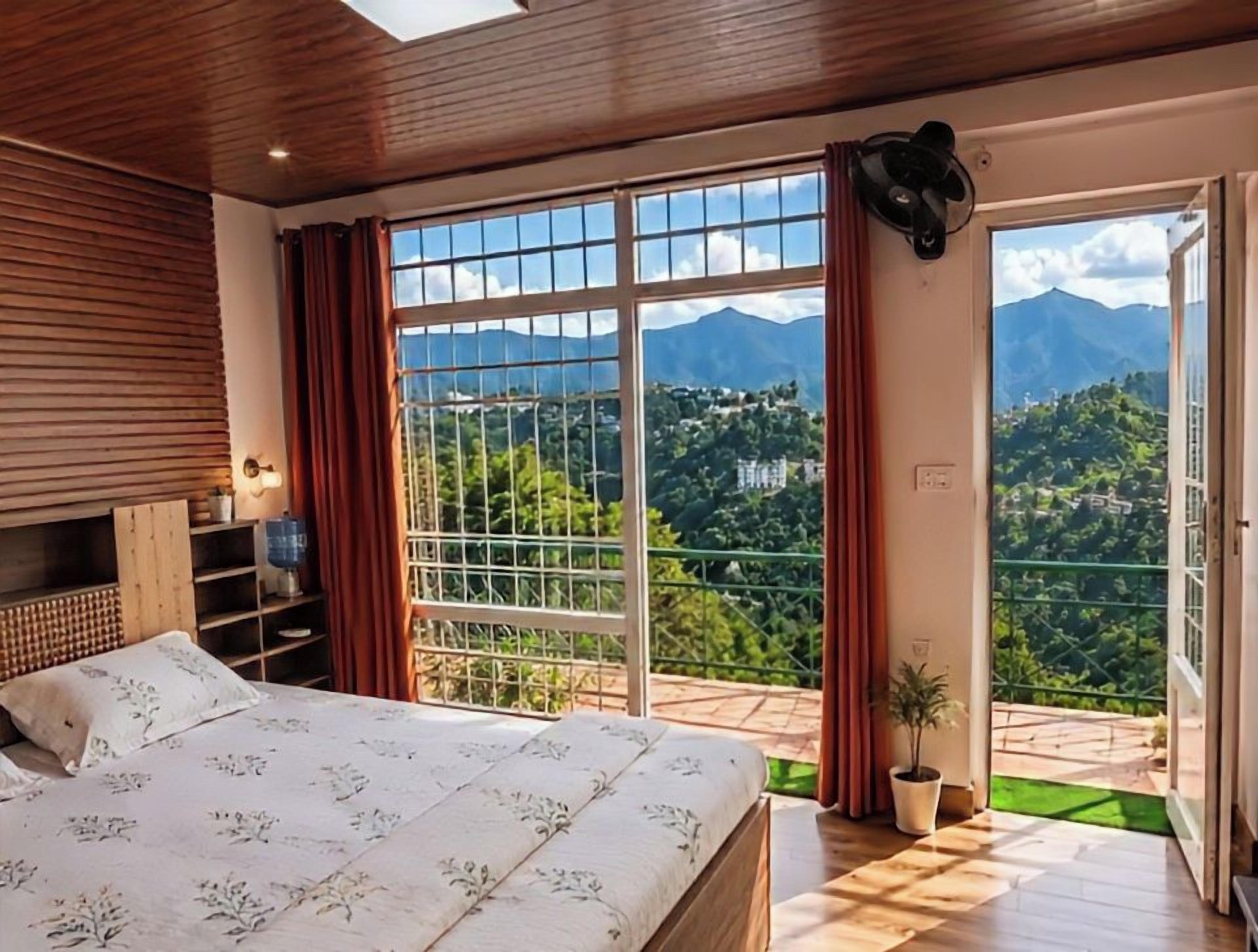 A bedroom with a large bed, wooden headboard, a view of mountains, and a balcony with a potted plant.