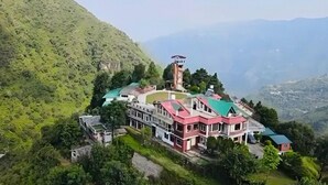 Un grande edificio a più piani con una torre centrale, circondato da vegetazione lussureggiante e montagne sullo sfondo.