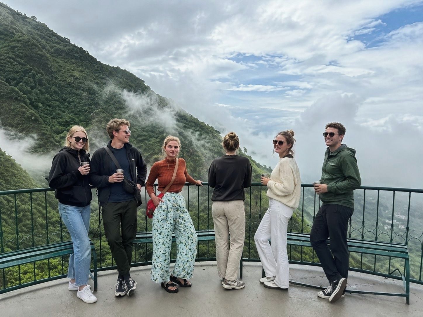 A group of people standing on a balcony with a mountainous landscape in the background.