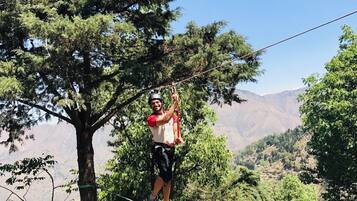 A person on a rope bridge in a natural setting with trees and mountains in the background.