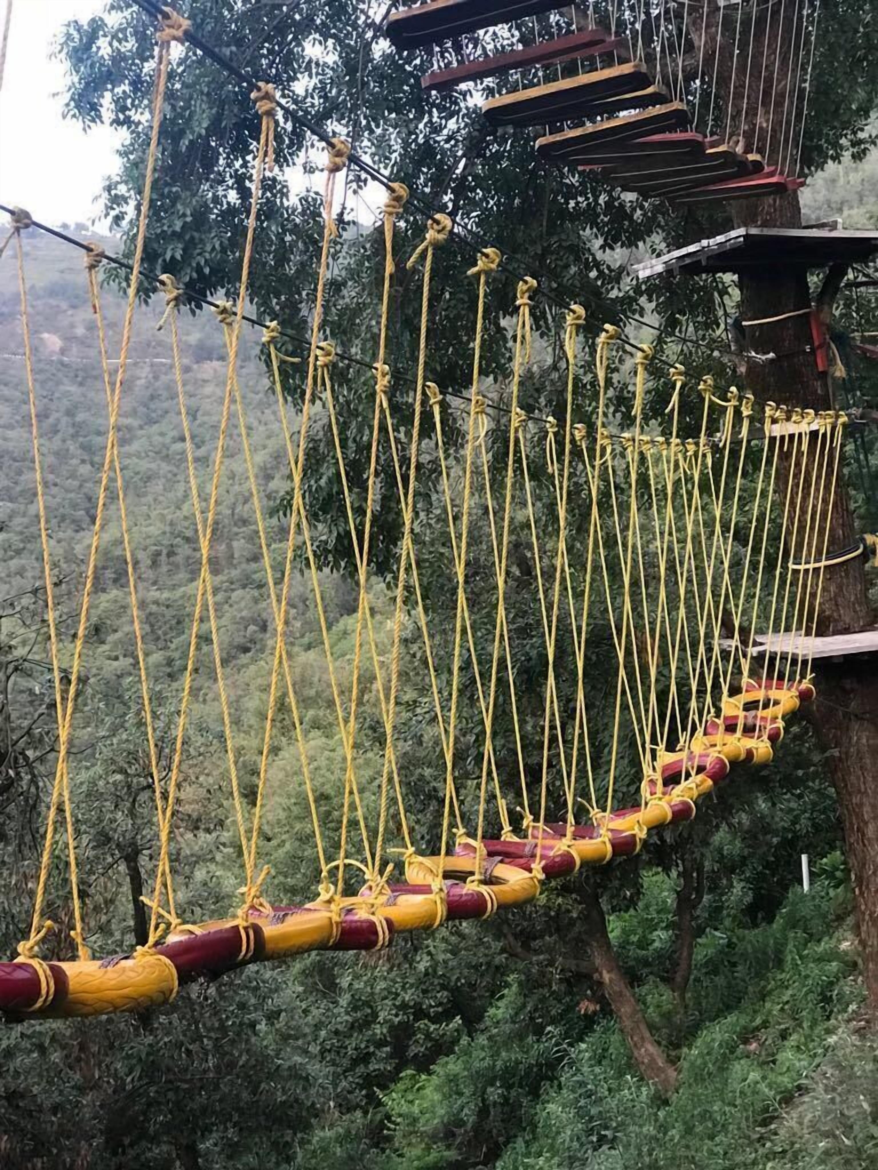 A rope bridge with yellow ropes and red and yellow padded steps.