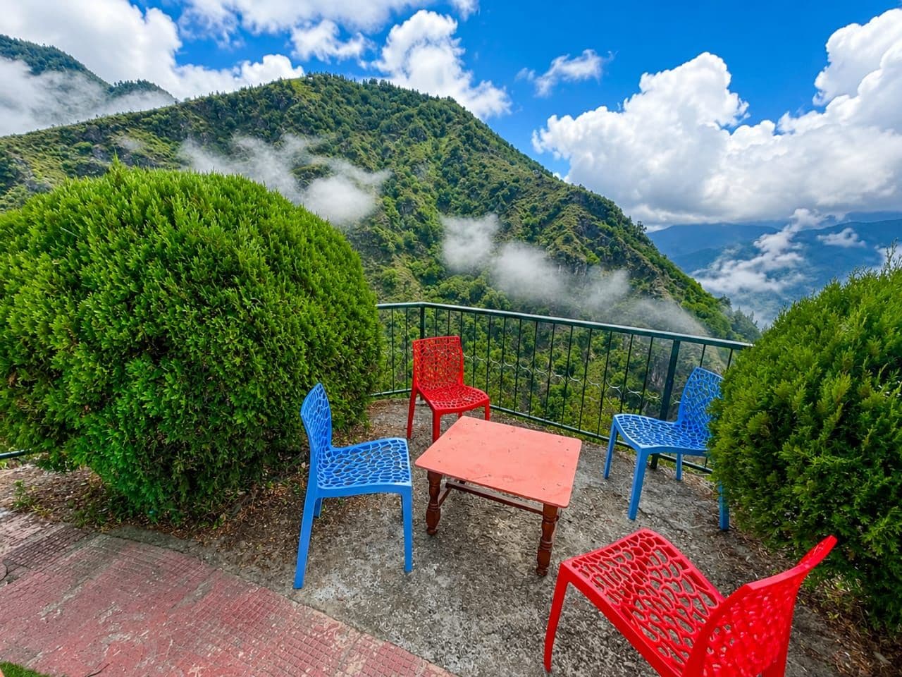 A terrace with a table and chairs, surrounded by greenery and overlooking a mountainous landscape.
