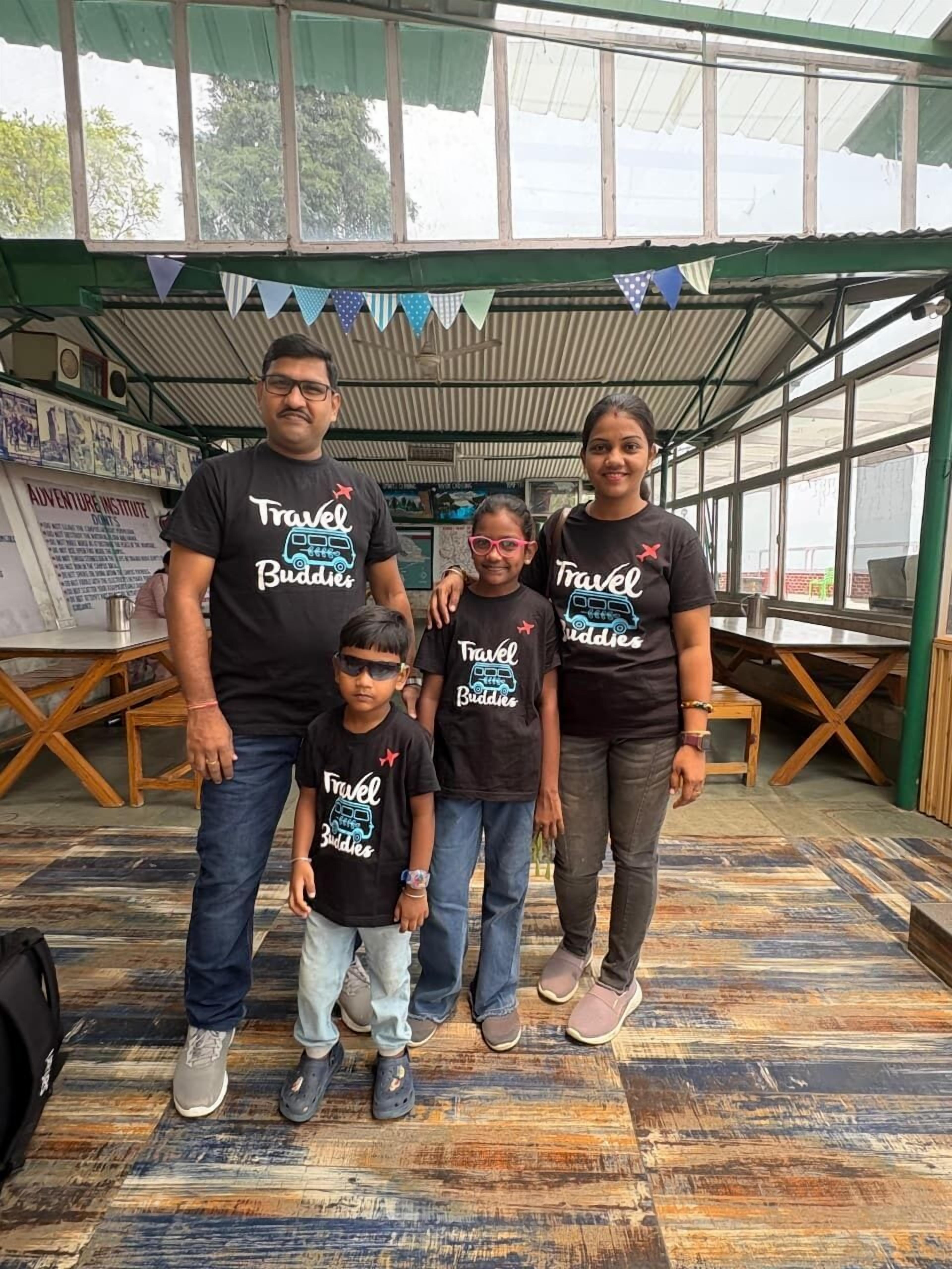 A family in a covered outdoor area with a tiled floor, a green roof, and a banner overhead.