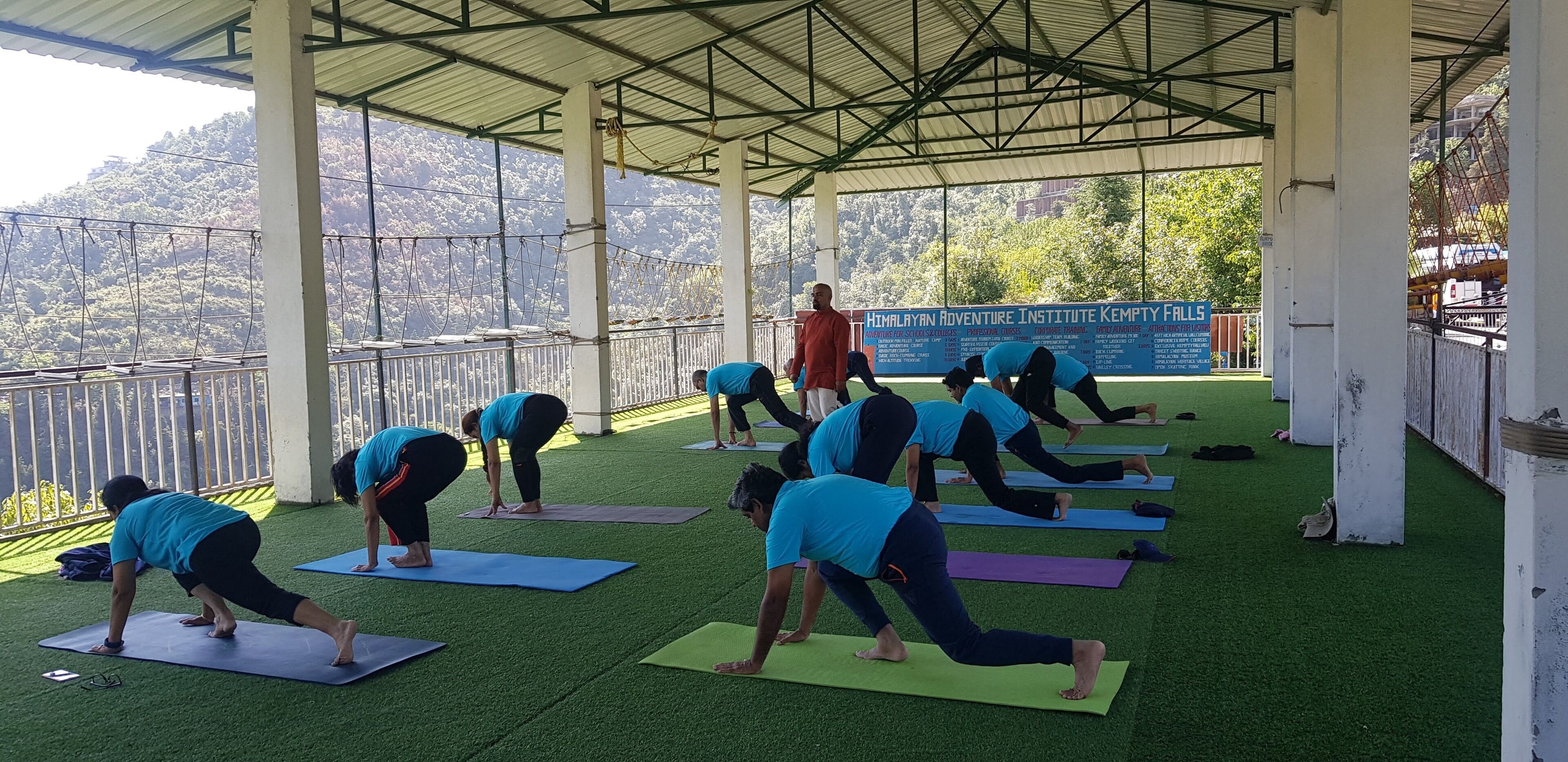 A group of people performing yoga on mats under a covered area with a view of a mountainous landscape.