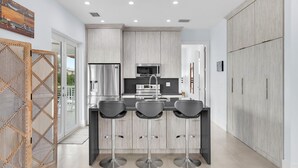 A modern kitchen with a central island, stainless steel appliances, and a view to the outside.