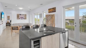 A modern kitchen with a central island, a dining area with a sofa and chairs, and a balcony with a view.