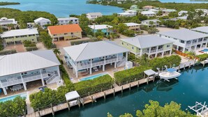 An aerial view of a coastal residential area with houses, a dock, and a swimming pool.