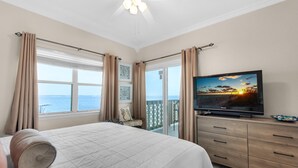 A bedroom with a bed, a television, a balcony with curtains, and a view of the sea. - Baywatch E3 (Pensacola Beach)