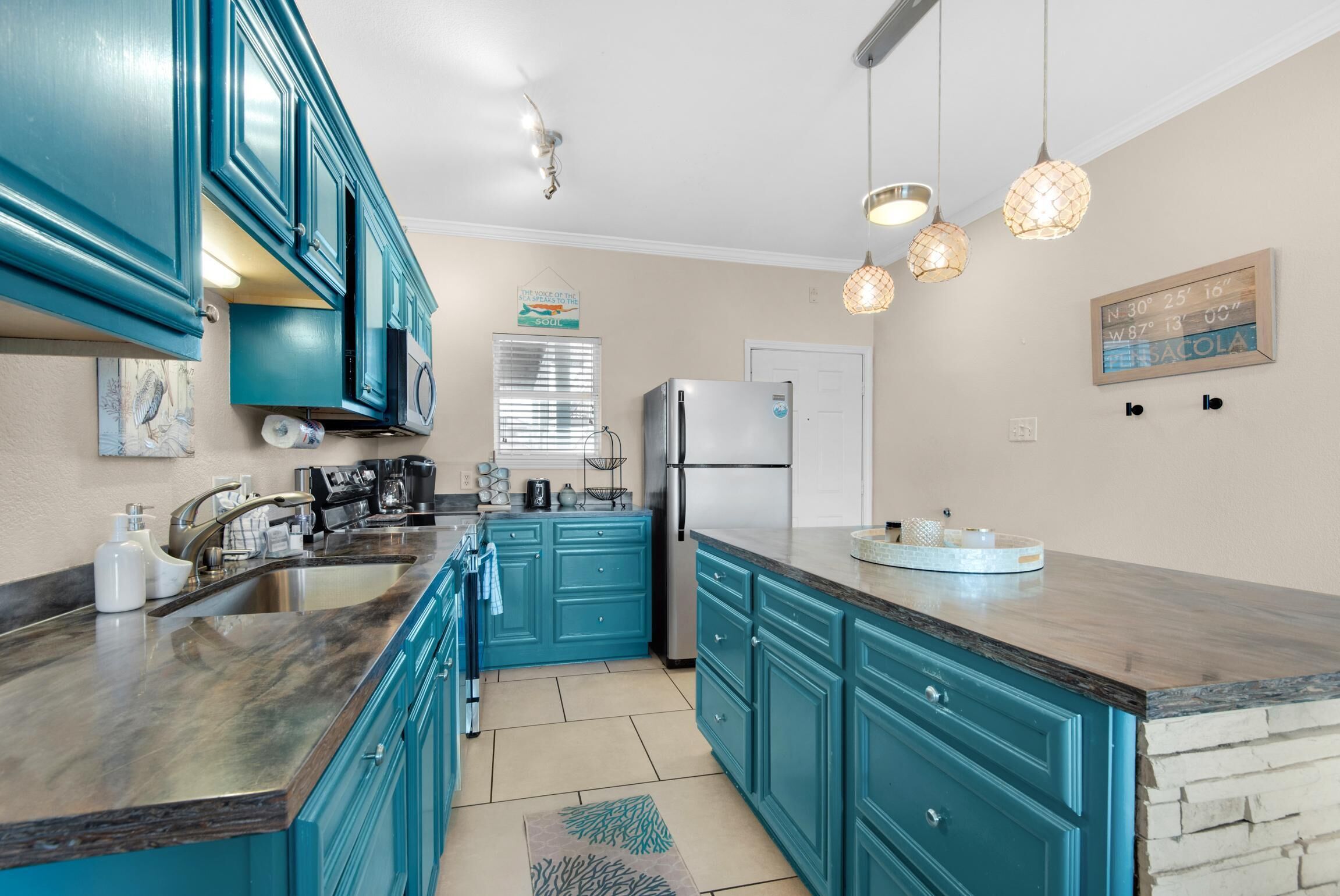 A kitchen with teal cabinets, a marble countertop, and a refrigerator.