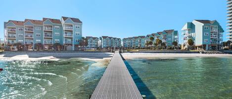 A waterfront hotel with a long pier leading to the beach, featuring multiple balconies and a clear view of the ocean.