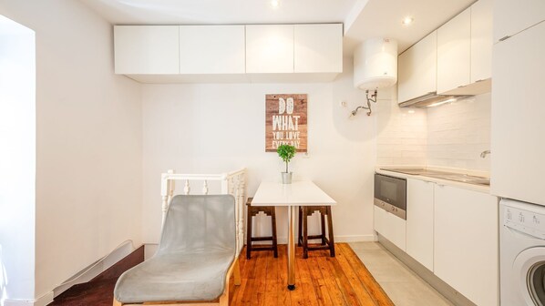 A compact kitchen with white cabinetry, a dining area with a table and chairs, and a built-in oven.