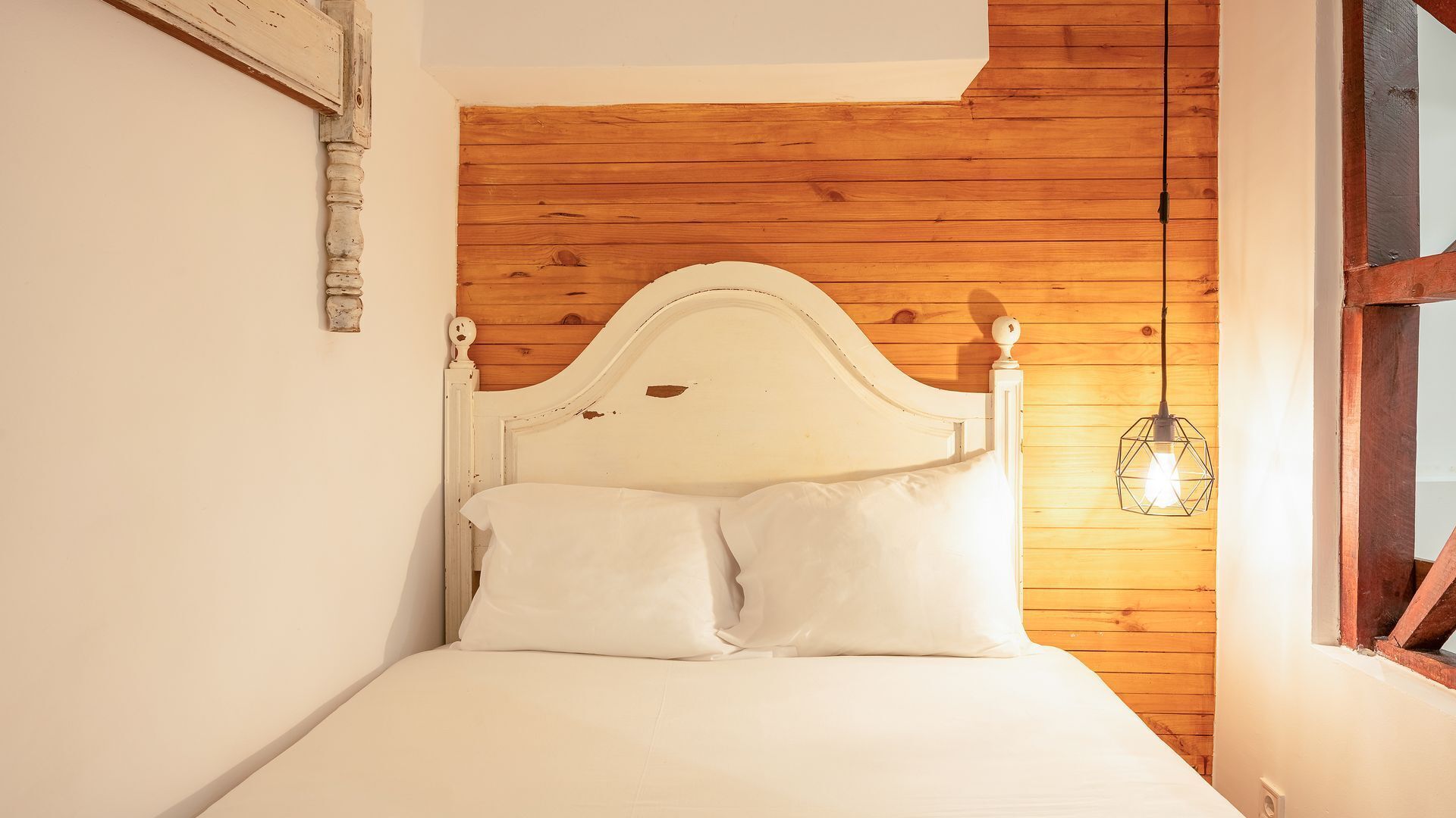 Un lit simple avec une tête de lit blanche et deux oreillers, placé contre un mur en bois avec un plafond en pente.