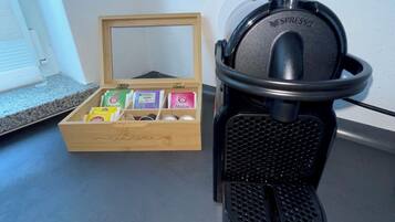 Una macchina da caffè Nespresso su un piano di lavoro, accanto a una scatola di legno con cialde per caffè.