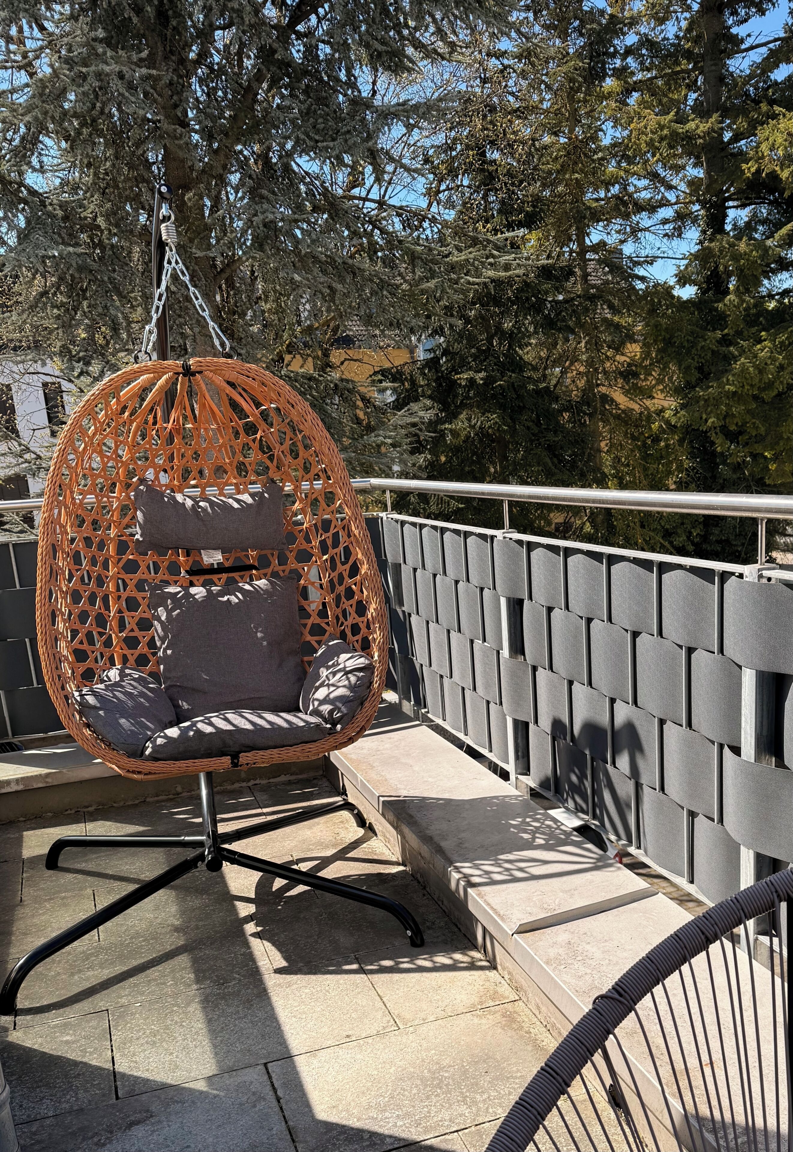 A wicker hanging chair with cushions on a balcony with a metal railing and steps.