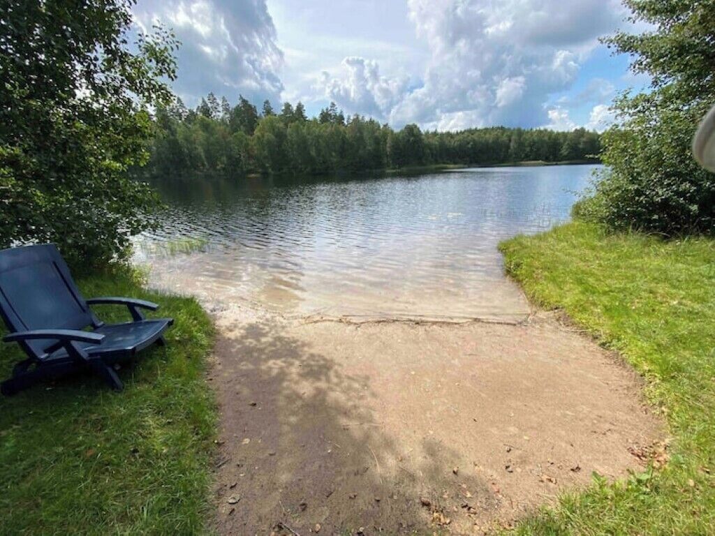 En stig som går längs sjön och leder till ett sandigt område med en stol, omgivet av grönska och träd.