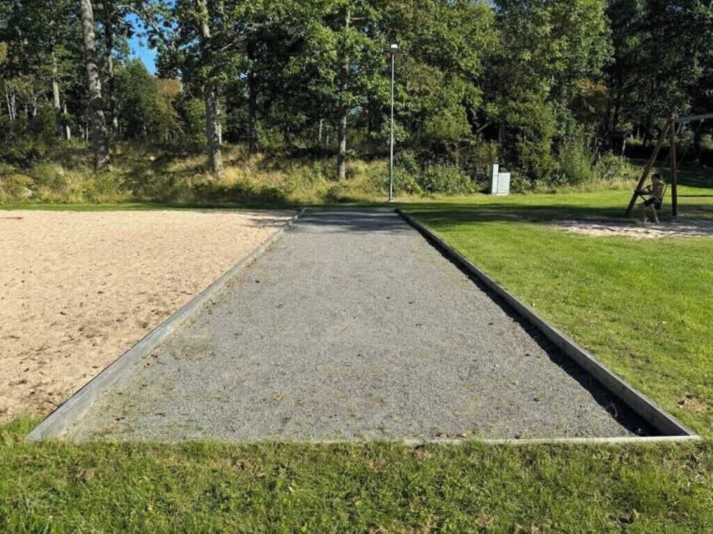 Ett rektangulärt område med grus, omgivet av en metallkant, gräs och träd.