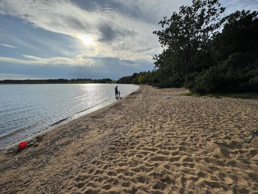 En strand med en person som går, ett rött föremål i sanden och ett kors i bakgrunden.