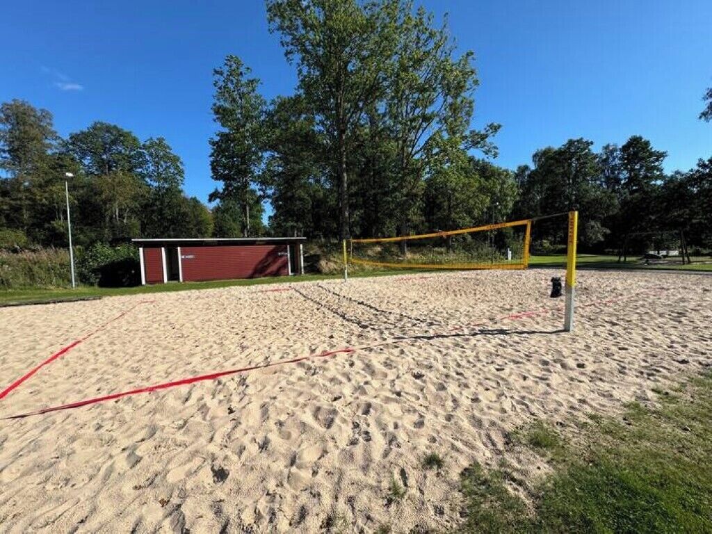 Ein Volleyballfeld mit Netz, umgeben von Sand und Bäumen.