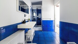 A modern bathroom with a white sink, blue-tiled walls, a glass shower enclosure, and a white door. - Suite in Colonne San Lorenzo Milano (Milan)
