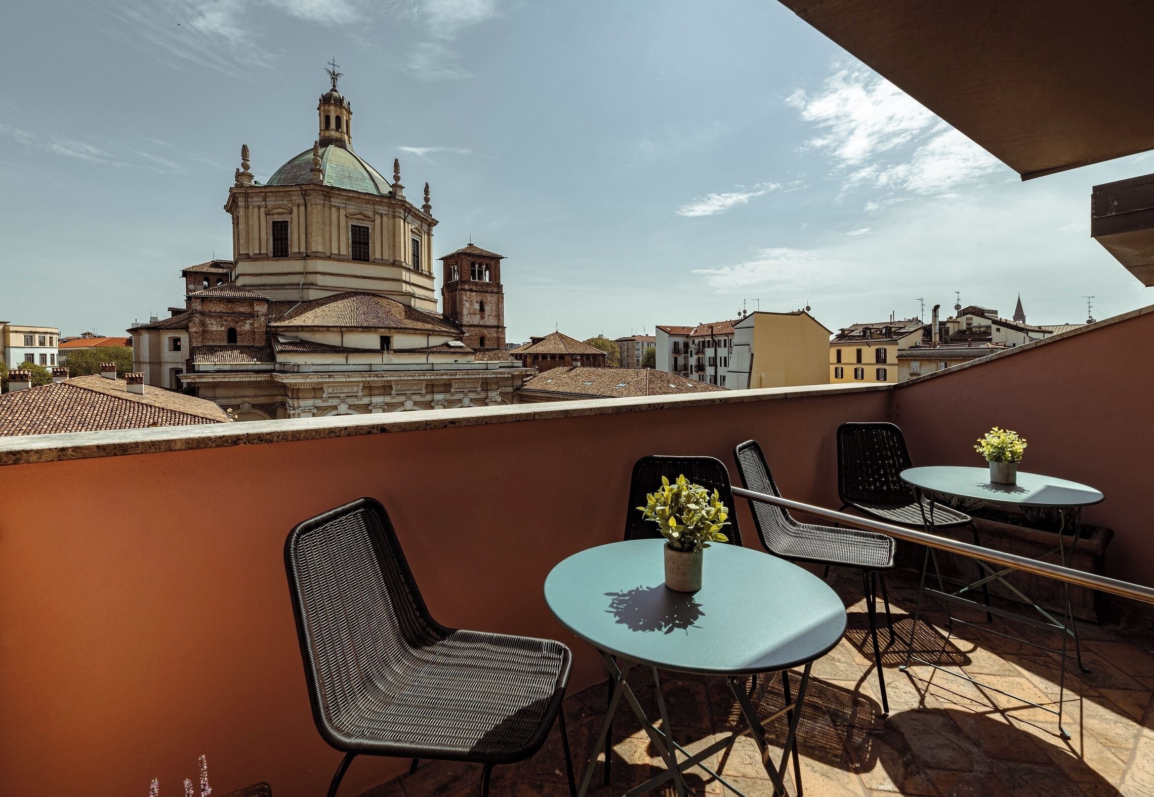 A terrace with two round tables and chairs, a potted plant, and a view of a historic building with a dome and bell tower.