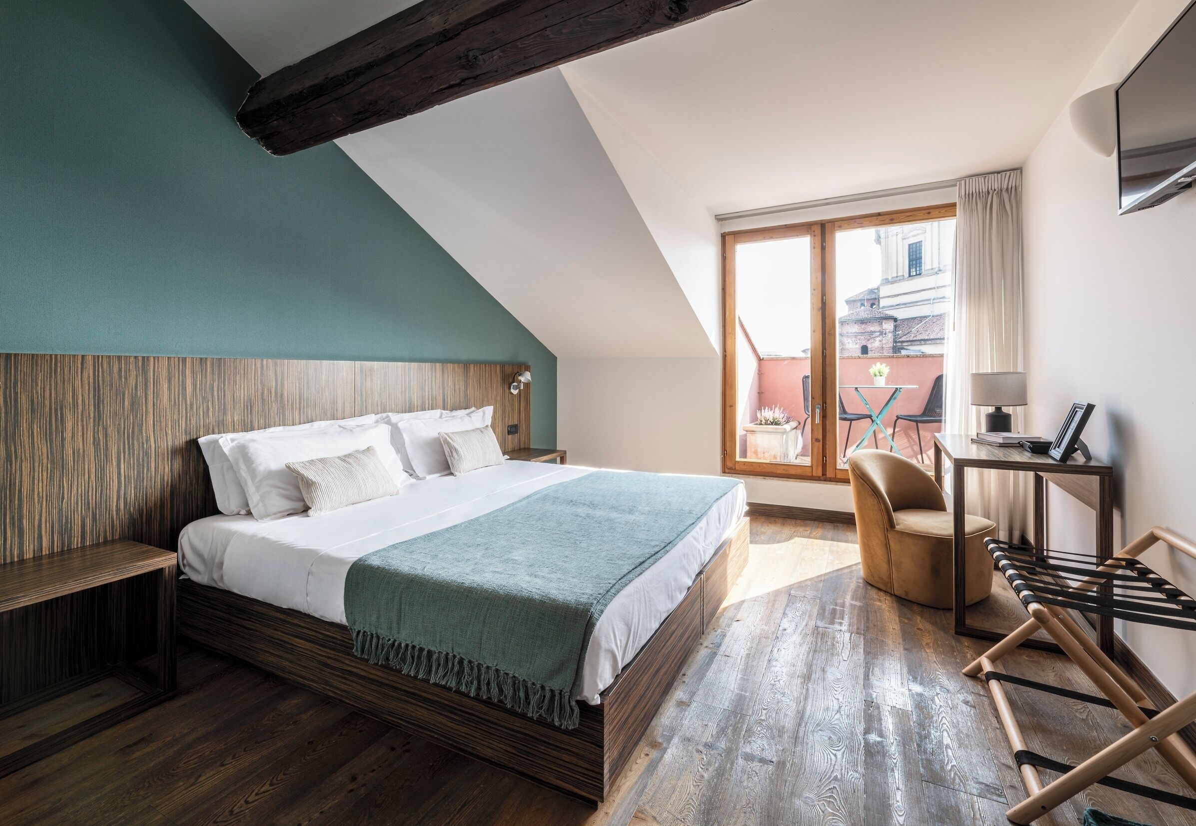 A bedroom with a wooden bed, a bench, a desk, and a view of the outside.