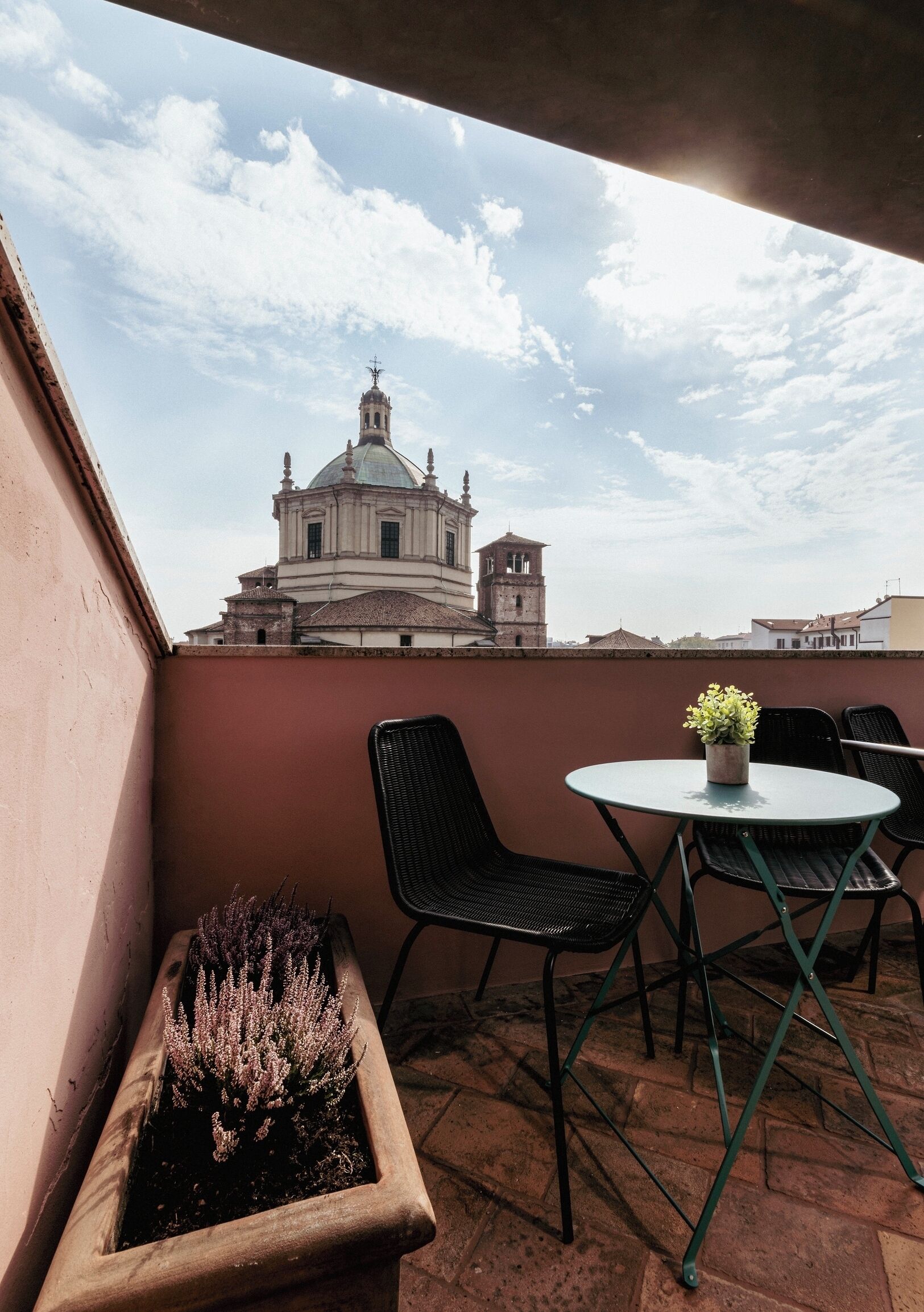 A balcony with a table and chairs, a potted plant, and a view of a historic building with a dome and bell tower.