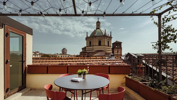 A rooftop terrace with a round table and red chairs, overlooking a historic building with a dome and bell tower. - Suite in Colonne San Lorenzo Milano (Milan)