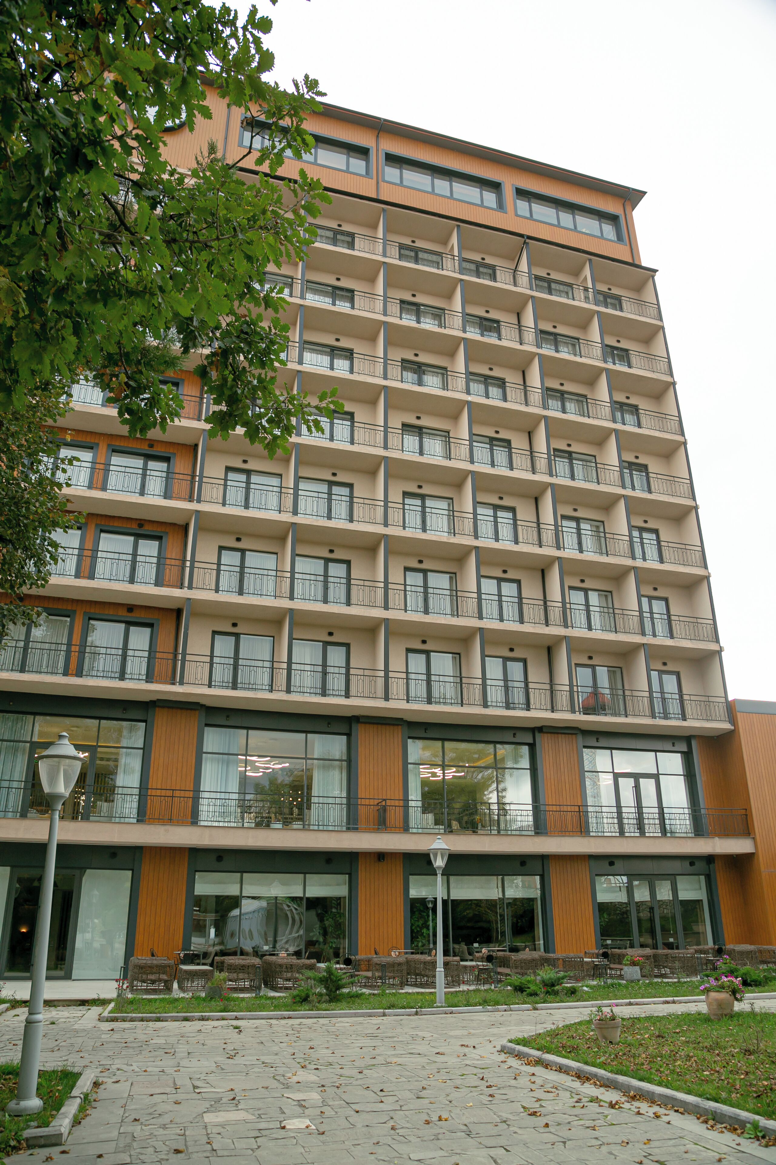 A multi-story building with balconies, large windows, and a paved area with outdoor seating.