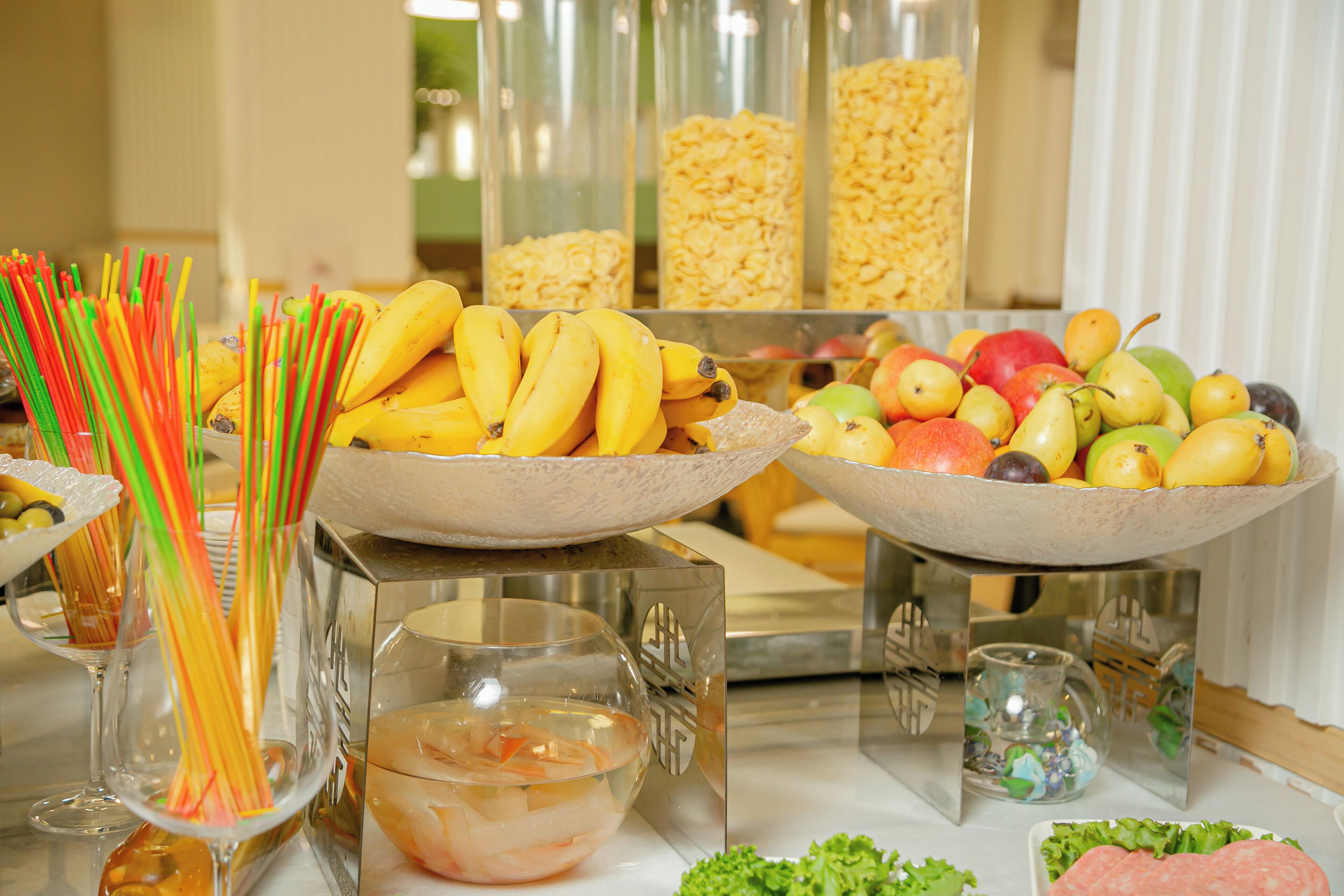 A buffet table with various food items including bananas, apples, pears, and shrimp.