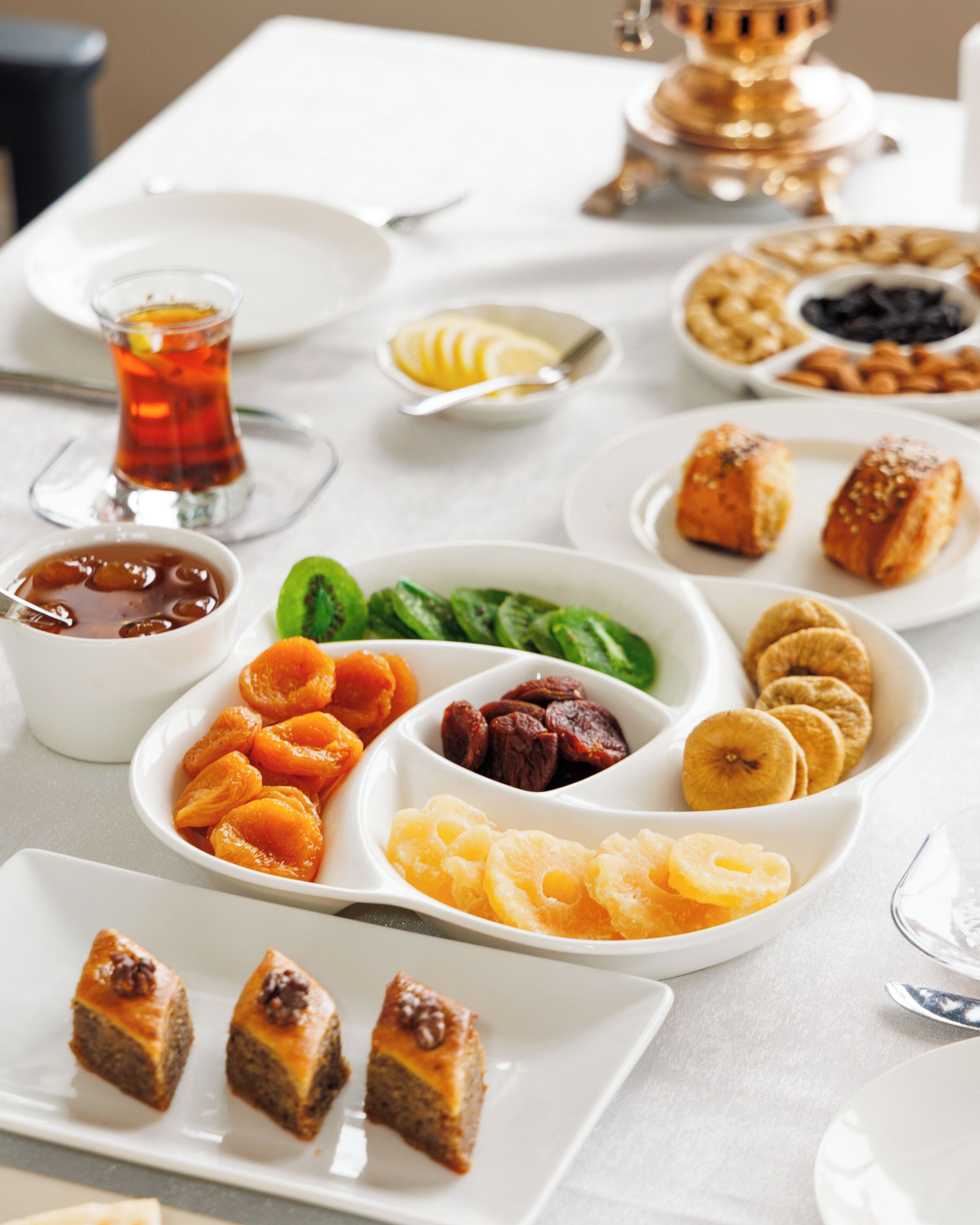 A table set with various dishes including pastries, fruits, and a glass of tea.