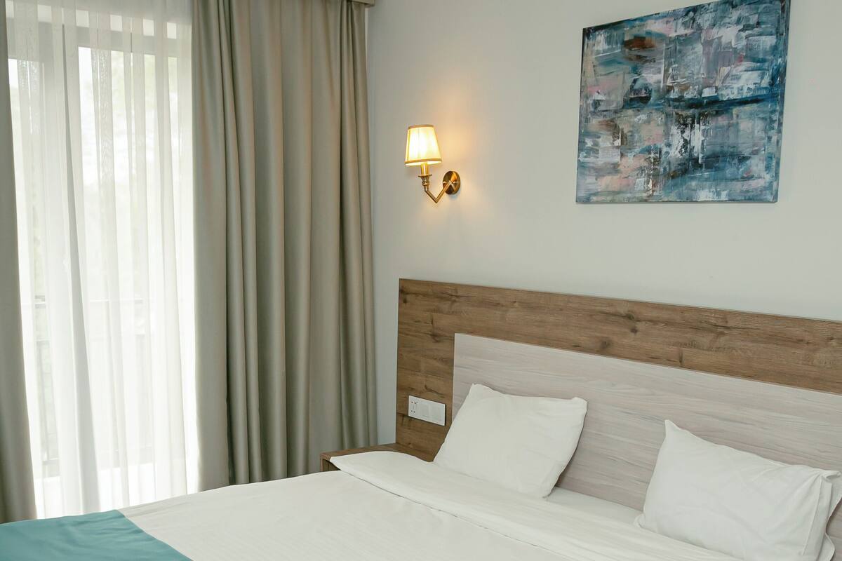 A hotel room with a large bed, a bedside table, a wall-mounted lamp, and a painting.
