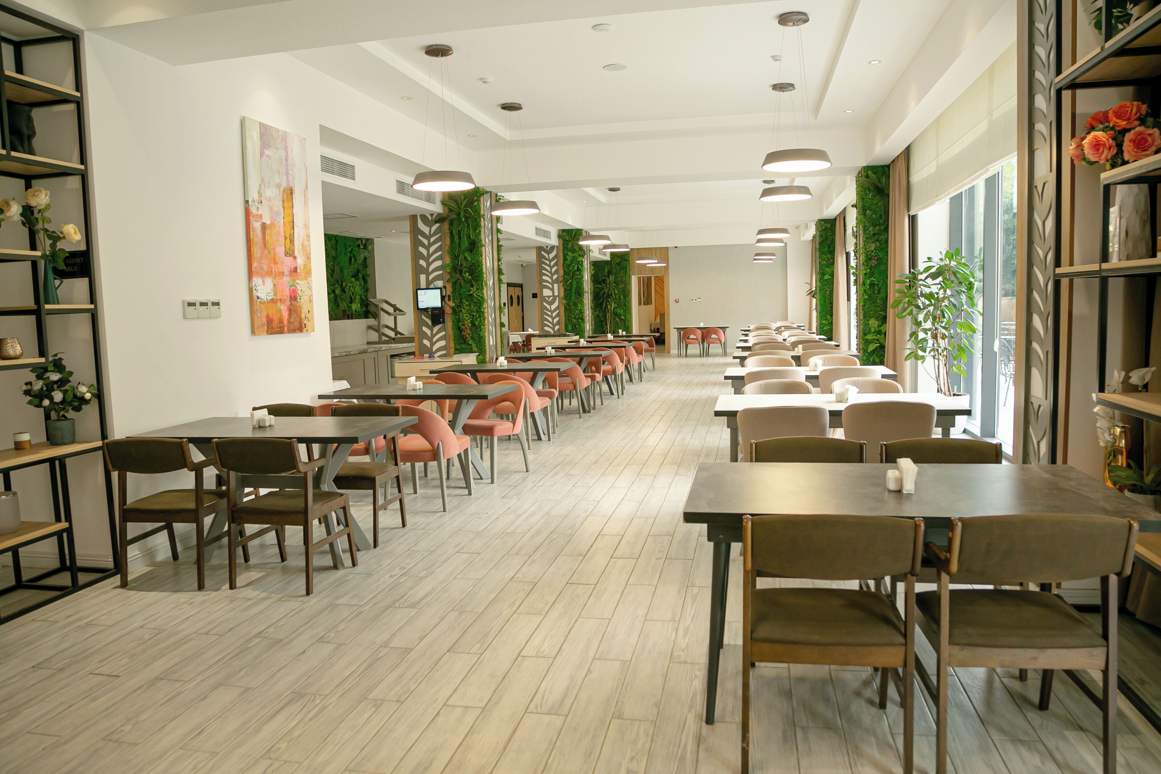 A spacious dining area with multiple tables and chairs, a modern ceiling design, and decorative plants.