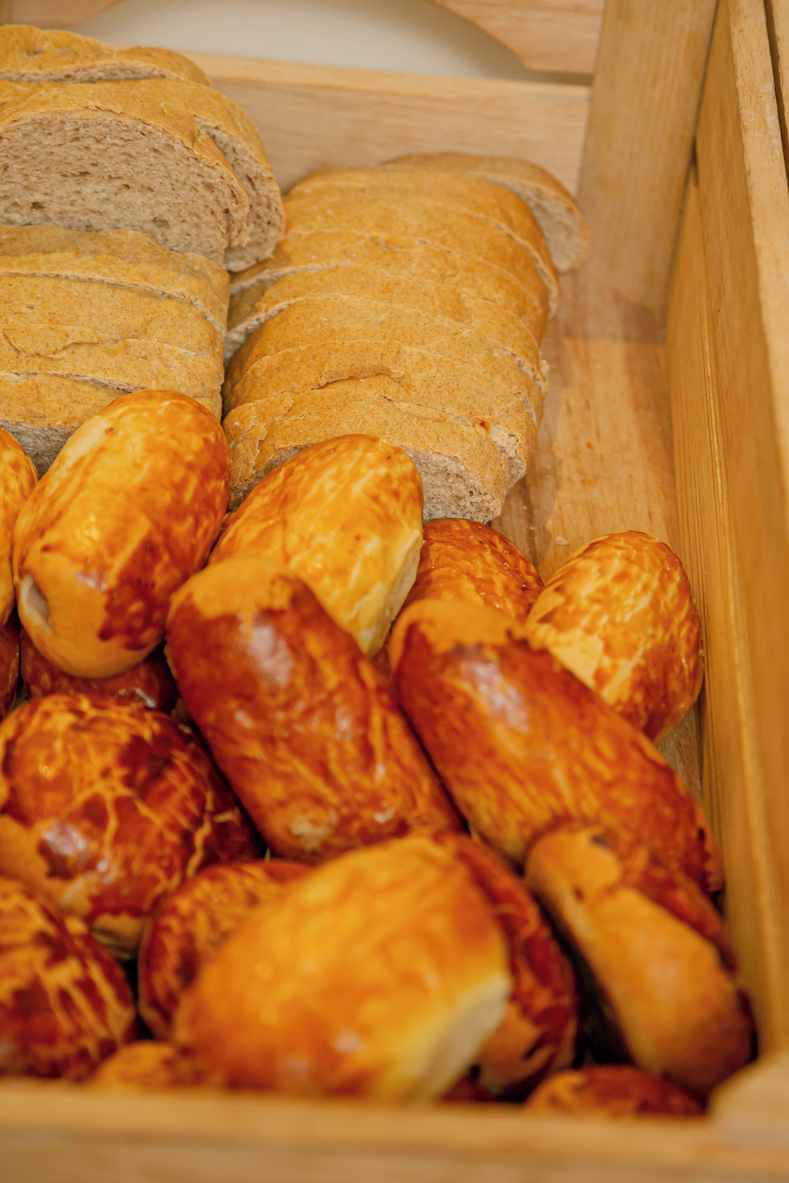A wooden box containing various types of bread, including baguettes and rolls.