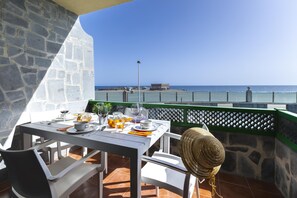 Un espacio de comedor al aire libre con una mesa lista para dos personas, con vista a una playa.
