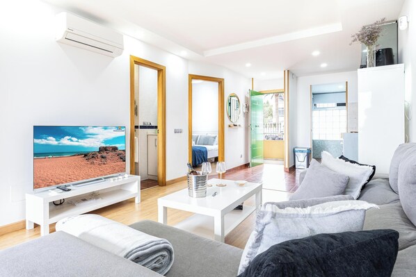 A modern living room with a television, sofa, coffee table, and a view of the beach.