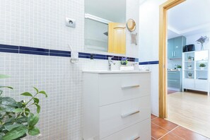 A modern bathroom with white tiled walls, a blue accent strip, a white vanity with drawers, a mirror, and a wooden door.