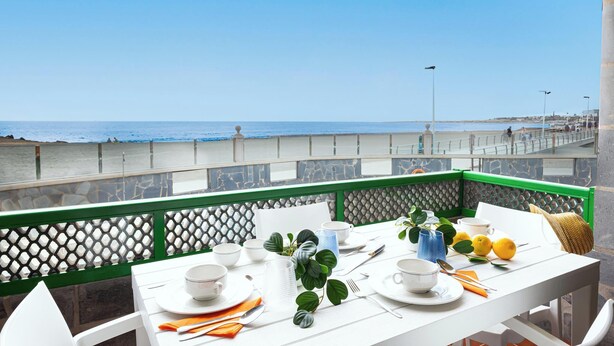 Una mesa dispuesta para comer con vista al mar, una barandilla verde y un muro de piedra.