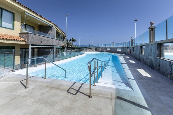 Una piscina con barrera de cristal, un flotador salvavidas y un cielo despejado.