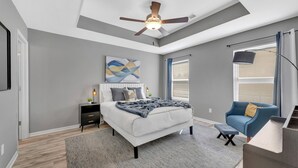 A bedroom with a bed, a nightstand, a blue chair, a ceiling fan, and a window with curtains.