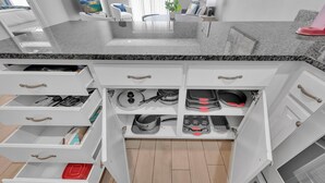 A kitchen with white cabinetry, granite countertops, and various kitchen utensils and cookware.