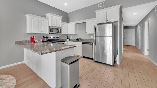 A modern kitchen with white cabinets, granite countertops, stainless steel appliances, and a wooden floor.