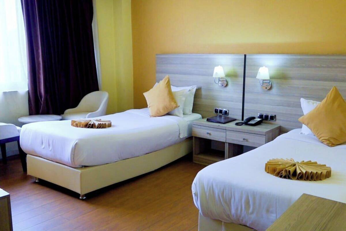 A hotel room with two beds, bedside tables, lamps, and a chair.