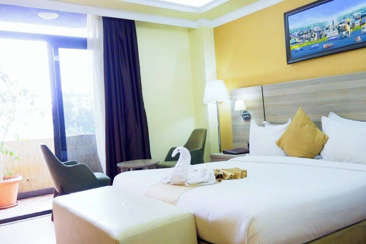 A hotel room with a large bed, a desk, a chair, a lamp, and a painting on the wall.