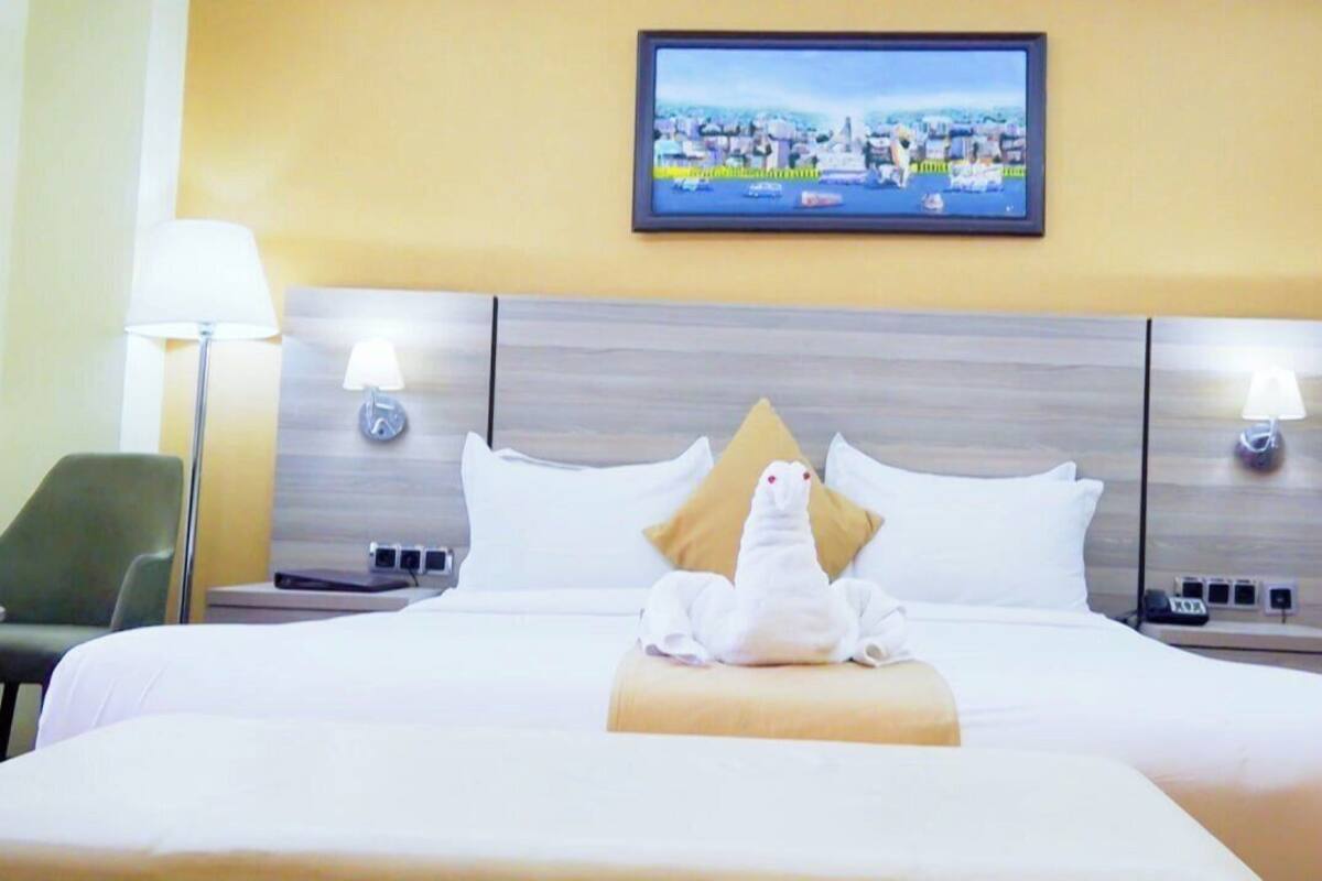 A hotel room with a bed, a flat-screen TV mounted on the wall, and a desk with a lamp.