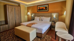 A hotel room with a large bed, a bedside table, a chair, a wardrobe, and a painting on the wall. - Holiday Hotel Addis Ababa (Addis Ababa)