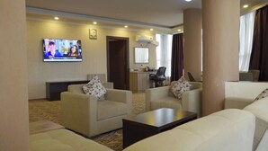 A hotel room with a living area featuring two sofas, a coffee table, a TV mounted on the wall, and a small kitchenette. - Holiday Hotel Addis Ababa (Addis Ababa)